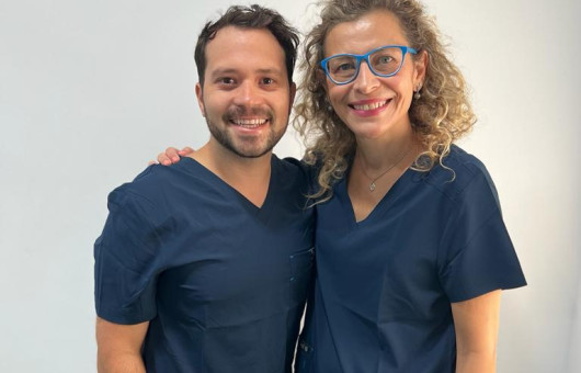 Dentiste français a l'étranger souriant tenant des instruments dentaires et une brosse à dents, prêt pour un examen oral.