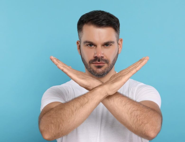 Un homme fait un signe de croix avec ses bras, représentant les choses interdites après une greffe de cheveux.