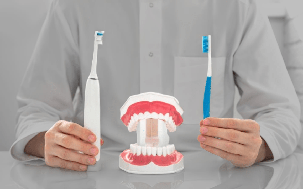 Un dentiste tenant une brosse à dents électrique et une brosse à dents manuelle avec une maquette de dents entre les deux.