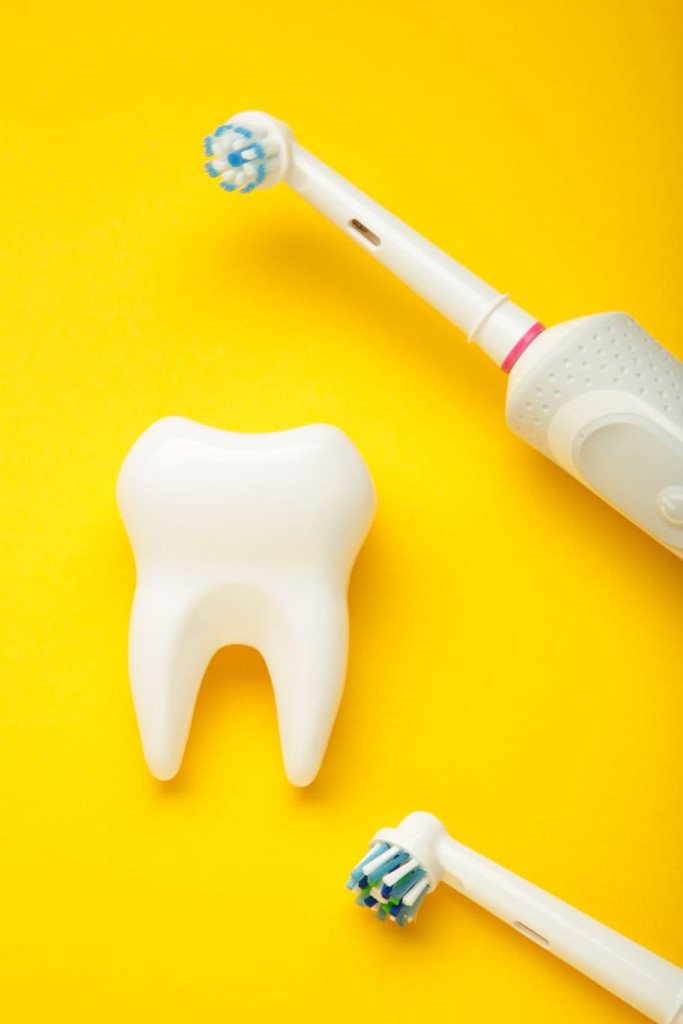 Brosse à dents électrique et dent en plastique sur fond jaune.